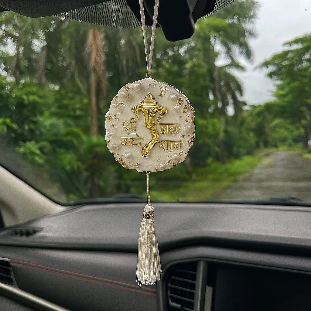 Decorative hanging charm on a car dashboard with a blurred green outdoor background