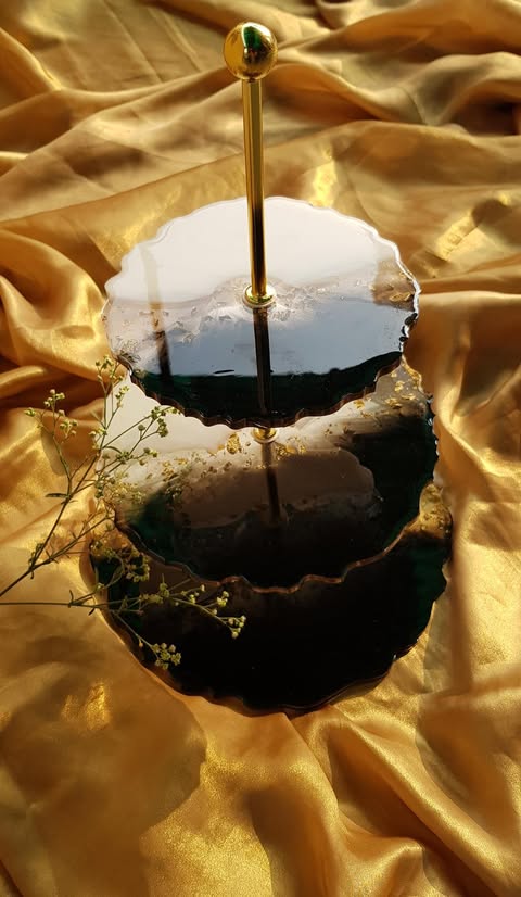 Three-tiered black cake stand with gold rod on a gold fabric background