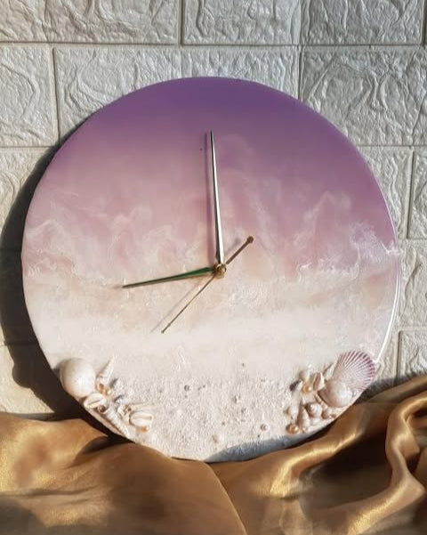 Round wall clock with a pink gradient and beach design, placed on a textured surface.