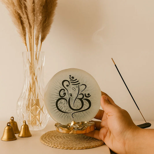 Decorative object with Ganesha Embedding held by a hand, next to a vase with dried plants and incense stick.