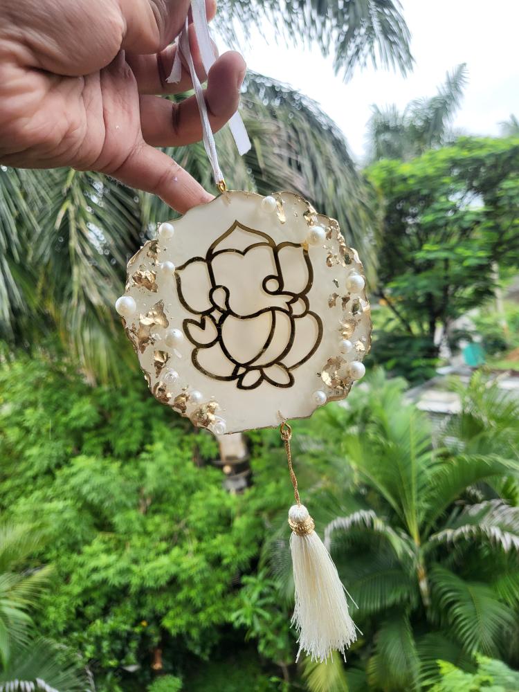 Decorative hanging ornament with Ganesha design held against a green outdoor background